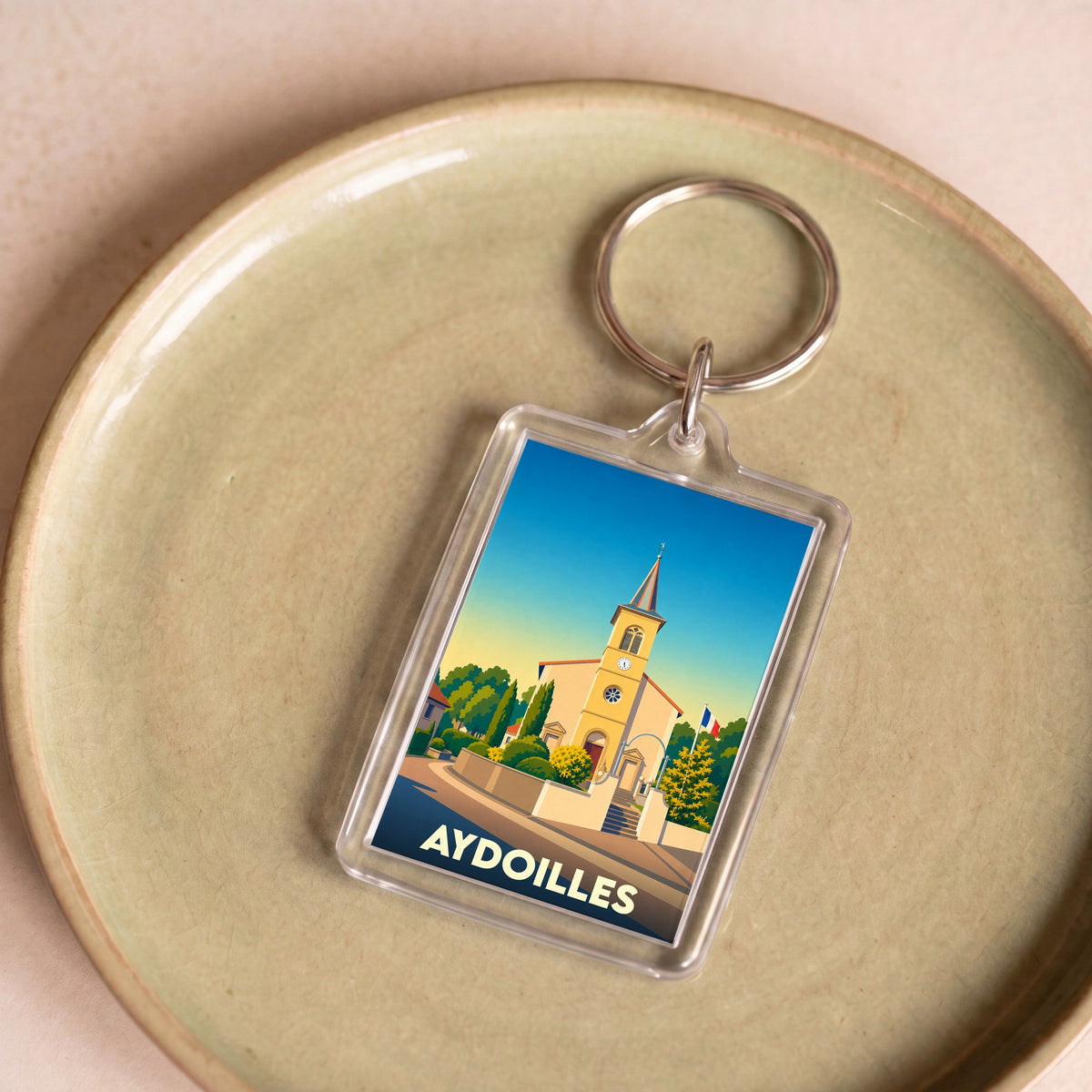 Porte-clés souvenir de la ville d'Aydoilles avec une illustration stylisée de son église.