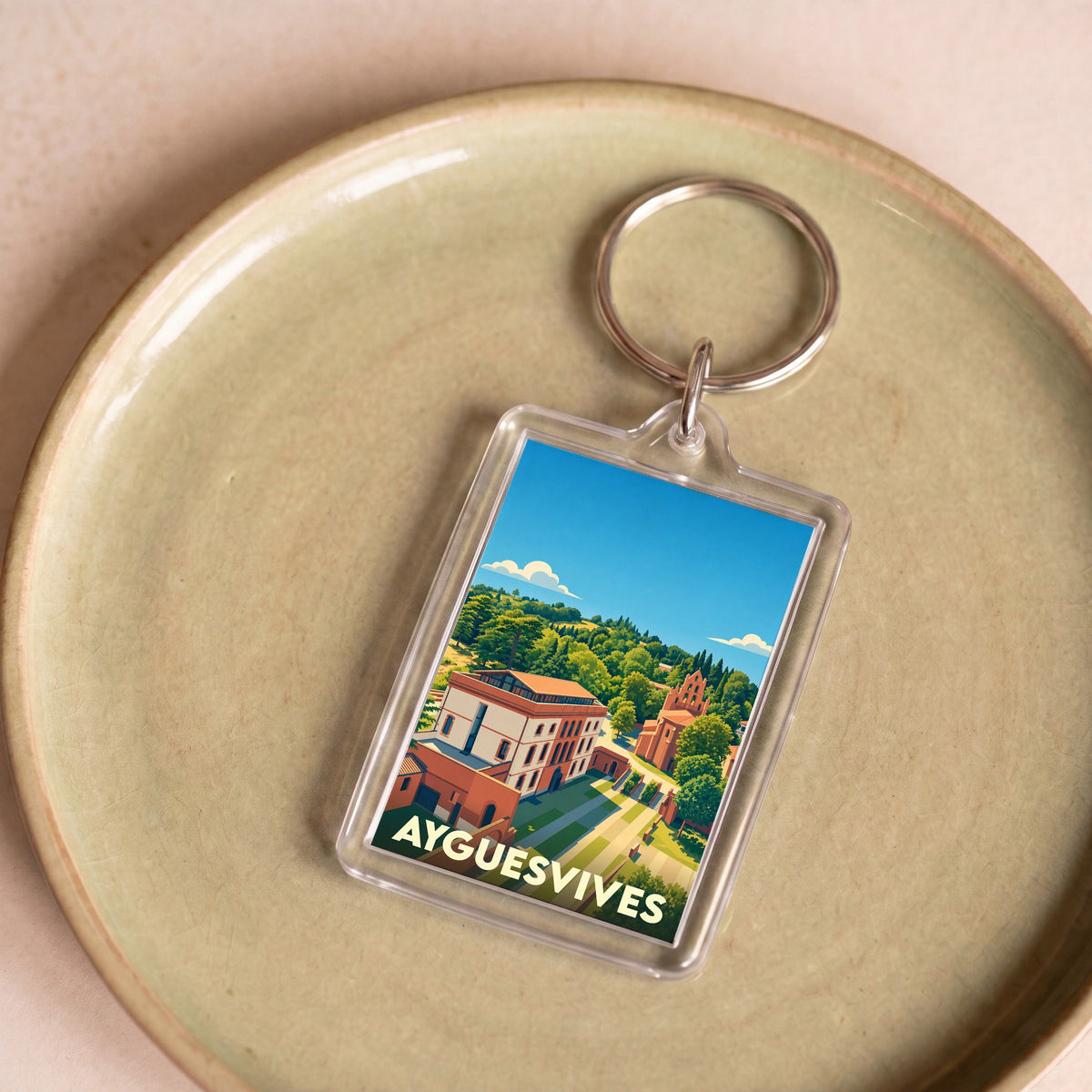 Porte-clés souvenir de la ville de Ayguesvives avec une illustration paysagère stylisée.