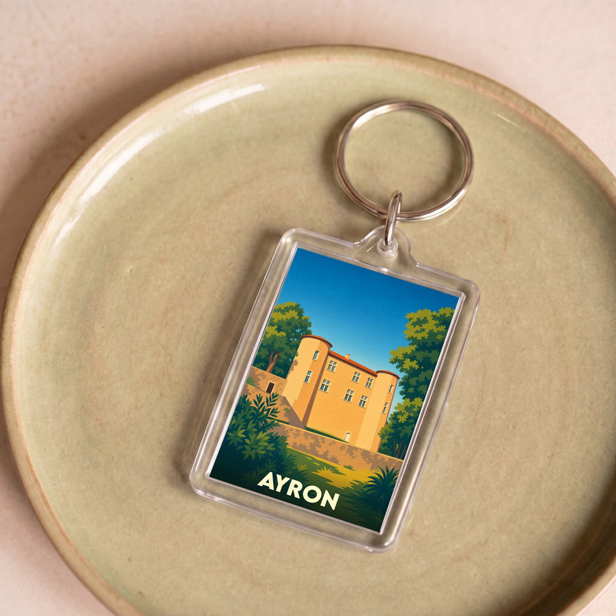 Porte-clés souvenir de la ville de Ayron avec une illustration stylisée du château local.