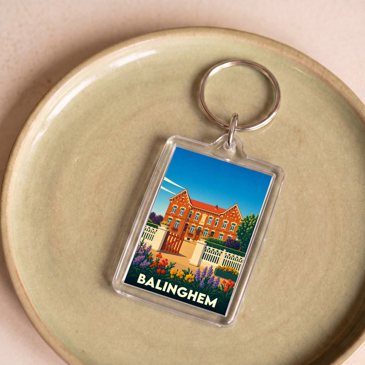 Porte-clés souvenir de la ville de Balinghem avec une illustration stylisée d'une grande maison bourgeoise.