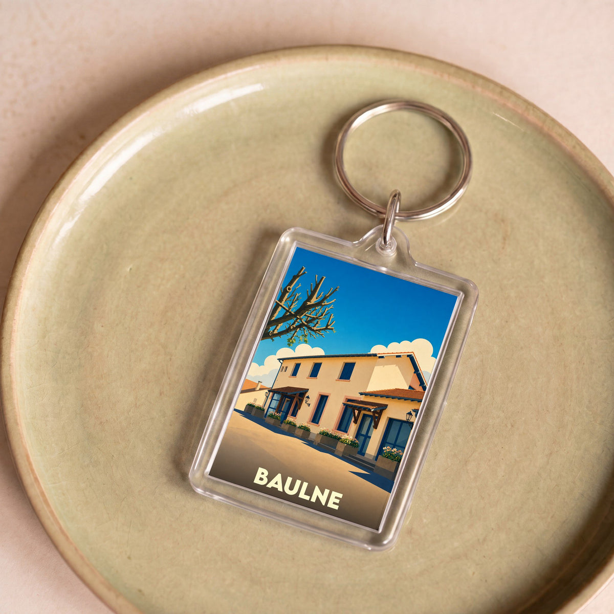 Porte-clés souvenir de la ville de Baulne avec une illustration stylisée d'un bâtiment ensoleillé.