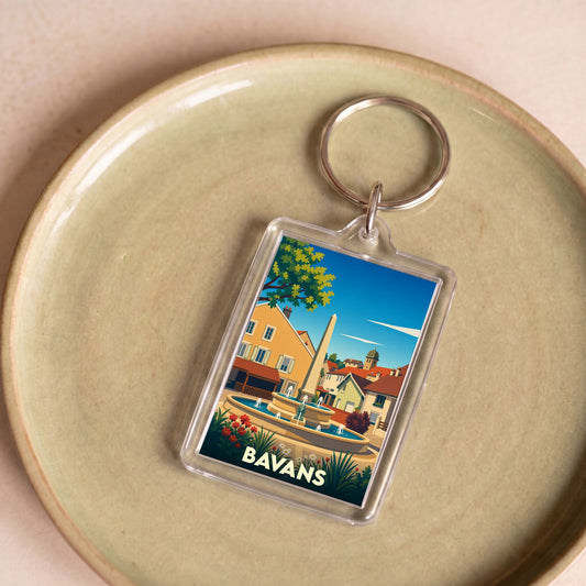 Porte-clés souvenir de la ville de Bavans illustrant une place ensoleillée avec une fontaine.