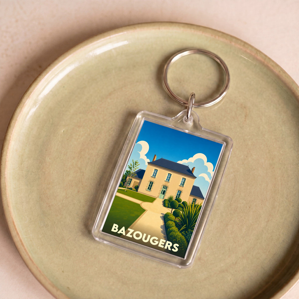 Porte-clés souvenir de la ville de Bazougers avec une illustration stylisée d'une demeure traditionnelle.