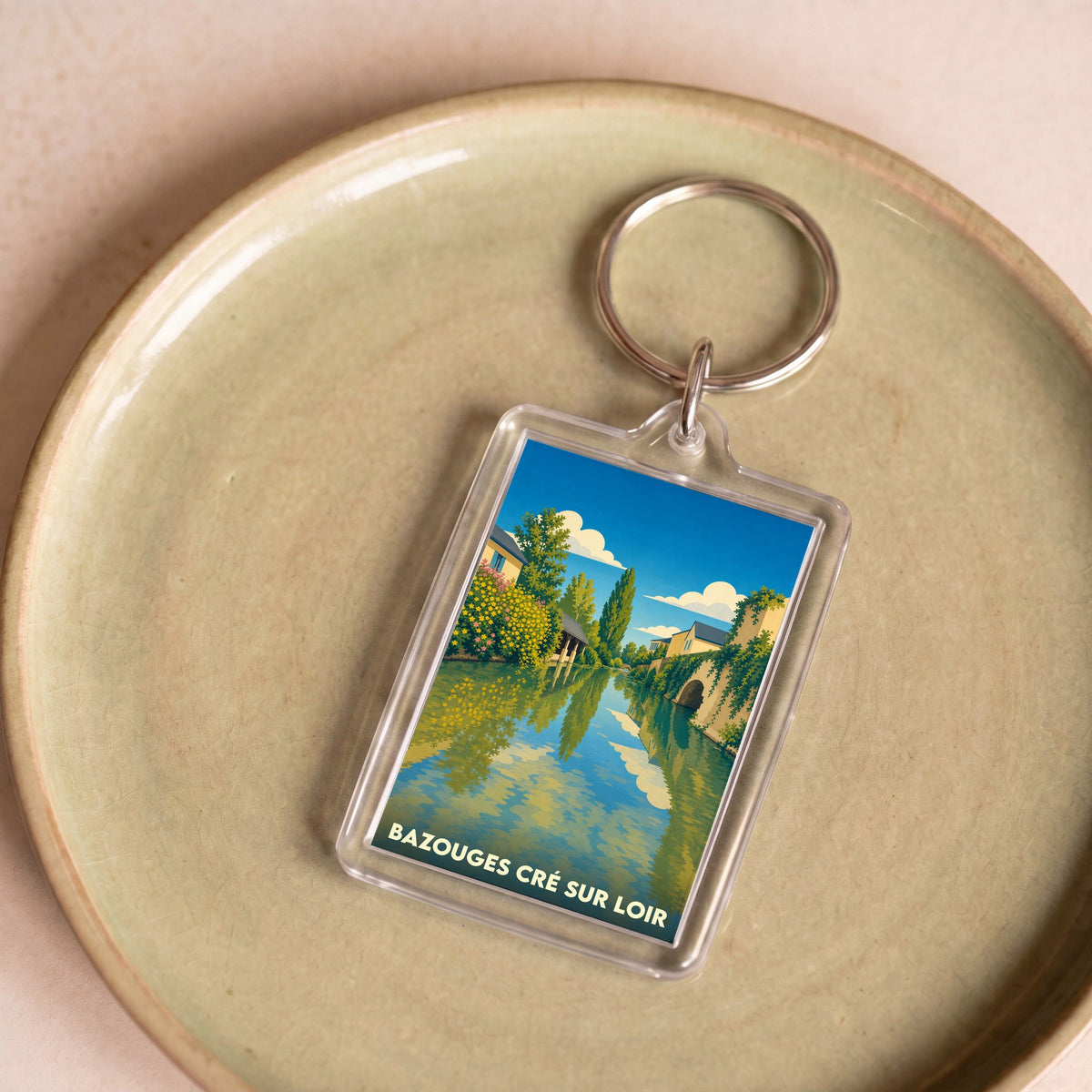 Porte-clés souvenir de la ville de Bazouges Cré sur Loir avec une illustration stylisée d'un paysage de rivière.