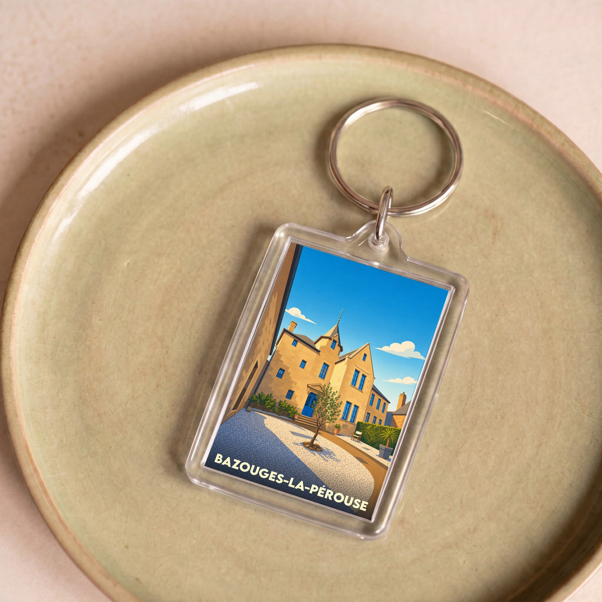 Porte-clés souvenir de la ville de Bazouges-la-Pérouse avec une illustration stylisée d'un bâtiment historique.