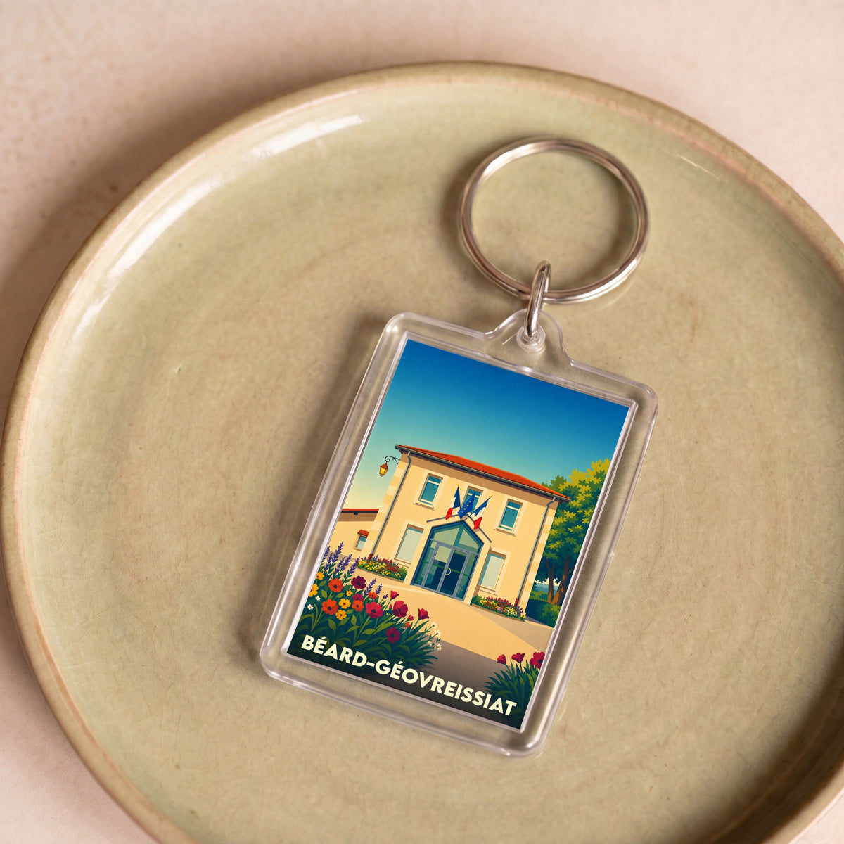 Porte-clés souvenir de la ville de Béard-Géovreissiat avec une illustration stylisée de sa mairie fleurie.