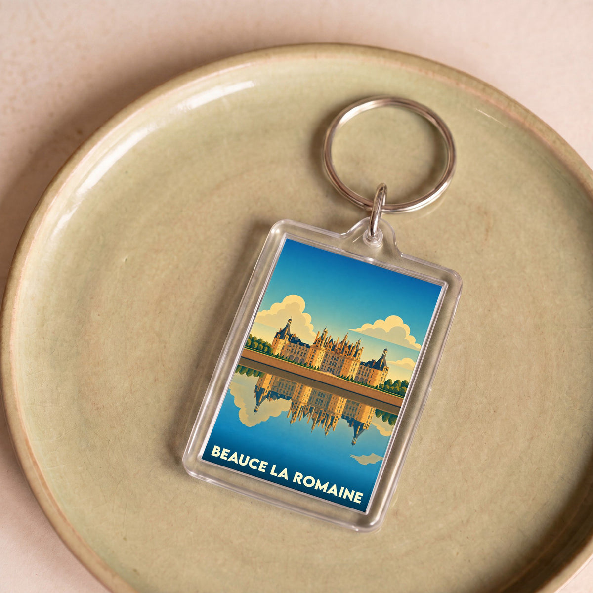 Porte-clés souvenir de la ville de Beauce la Romaine illustré par un château se reflétant sur l'eau.