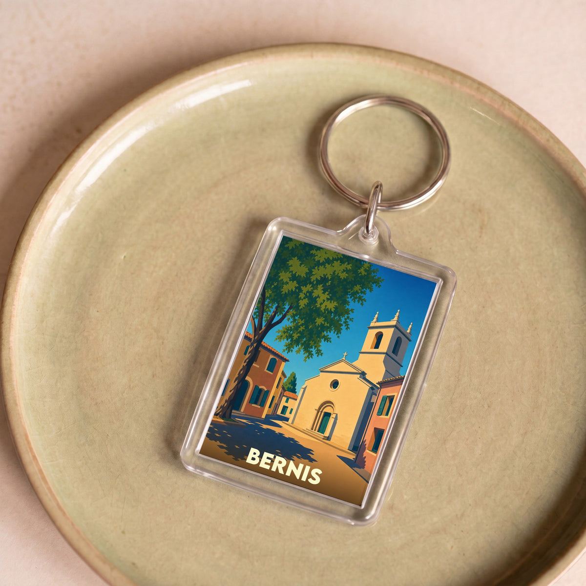 Porte-clés souvenir de la ville de Bernis avec une illustration stylisée d'une place ensoleillée.