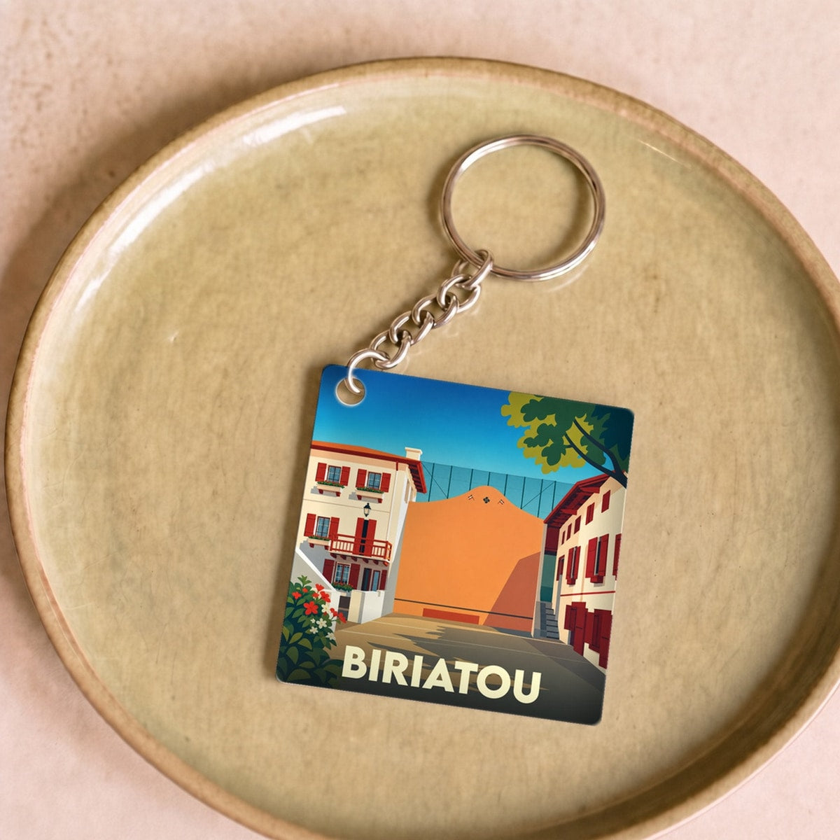 Porte-clés souvenir de la ville de Biriatou avec une illustration stylisée d'une place de village basque.