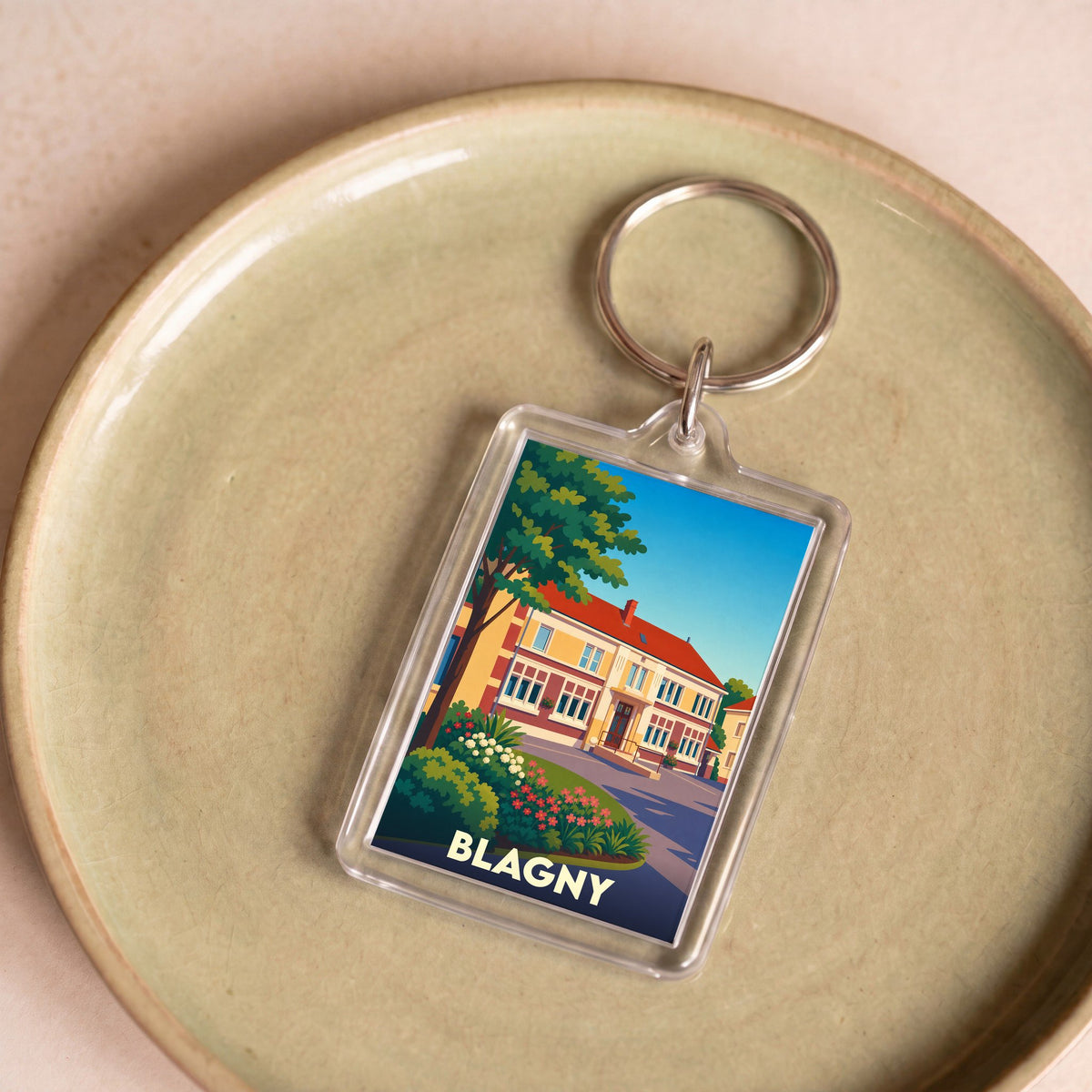 Porte-clés souvenir de la ville de Blagny avec une illustration stylisée d'une maison de maître fleurie.