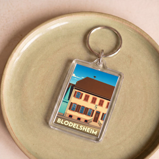 Porte-clés souvenir de la ville de Blodelsheim avec une illustration stylisée d'un bâtiment traditionnel.