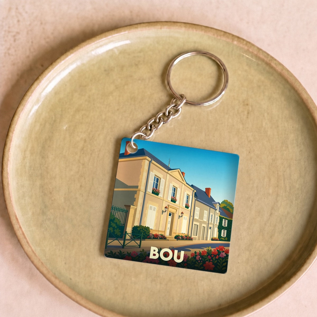 Porte-clés souvenir de la ville de Bou avec une illustration stylisée d'une rue fleurie.