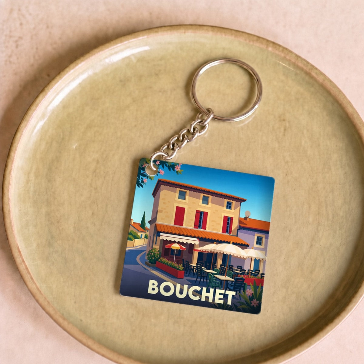 Porte-clés souvenir de la ville de Bouchet avec une illustration stylisée d'une terrasse de café.