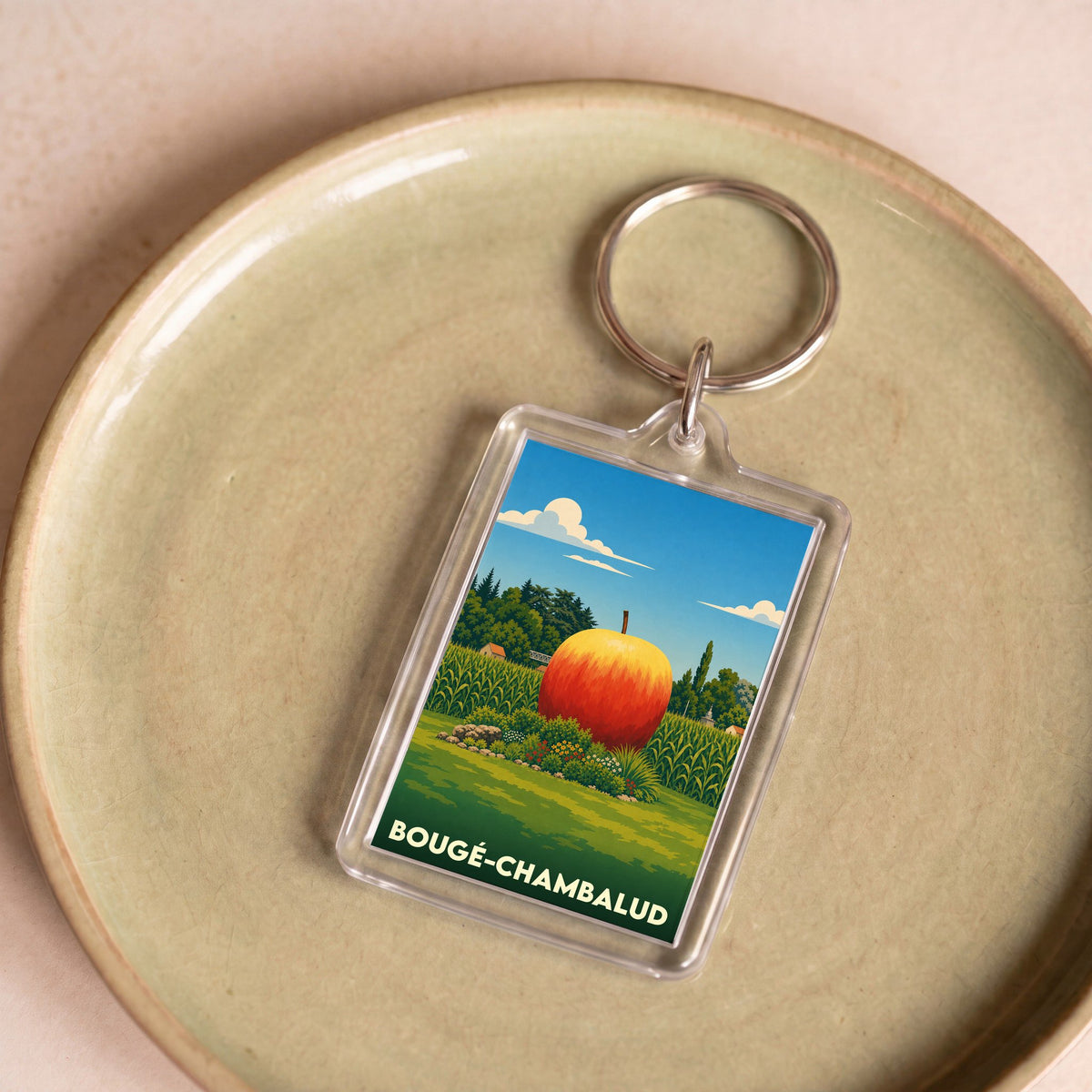 Porte-clés souvenir de la ville de Bougé-Chambalud avec une illustration stylisée d'une pomme géante dans un paysage rural.