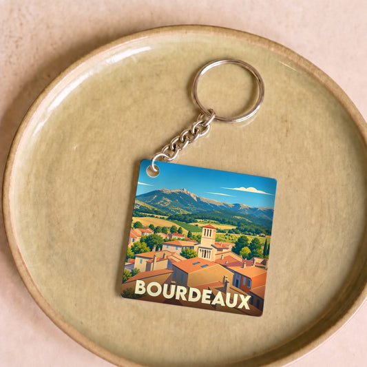 Porte-clés souvenir de la ville de Bourdeaux illustré d'un paysage provençal stylisé.