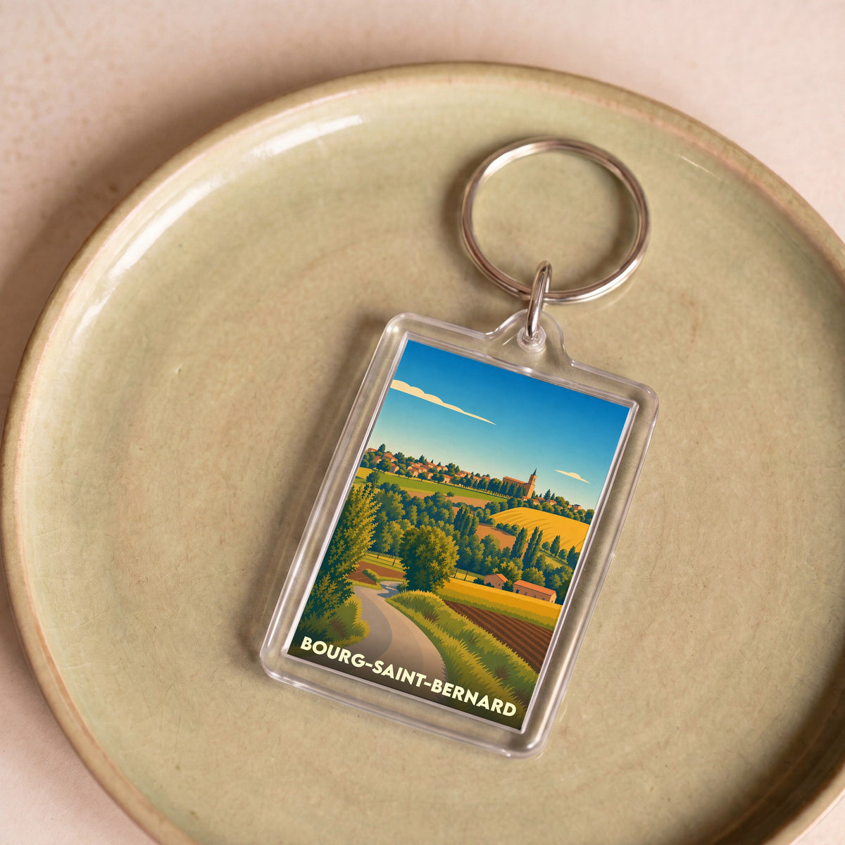 Porte-clés souvenir de la ville de Bourg-Saint-Bernard avec une illustration stylisée de son paysage vallonné.