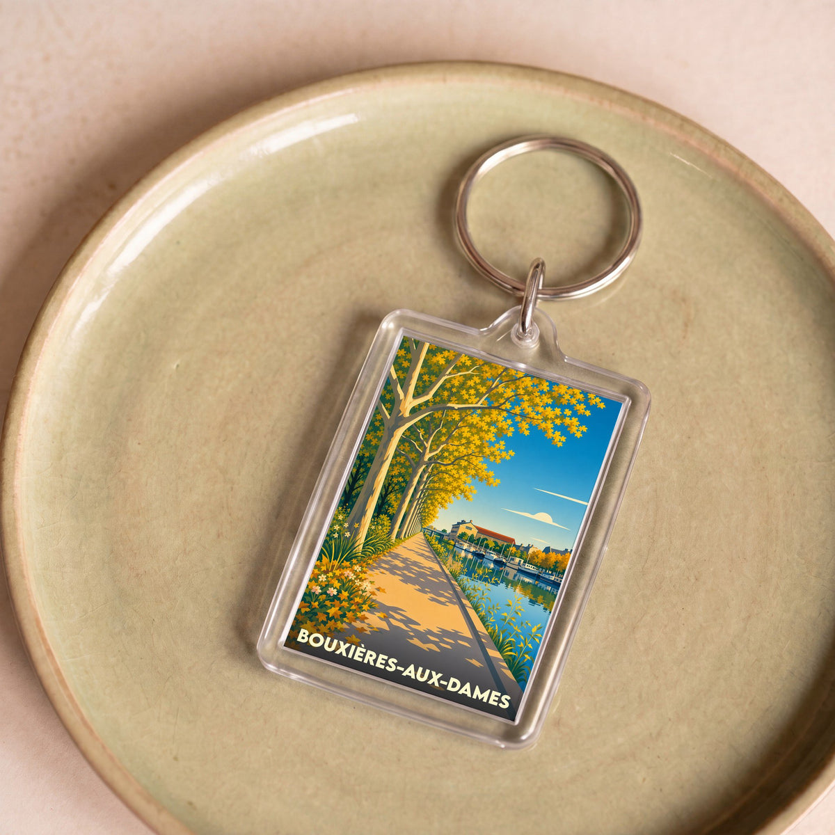 Porte-clés souvenir de la ville de Bouxières-aux-Dames avec une illustration stylisée d'un bord de rivière arboré.
