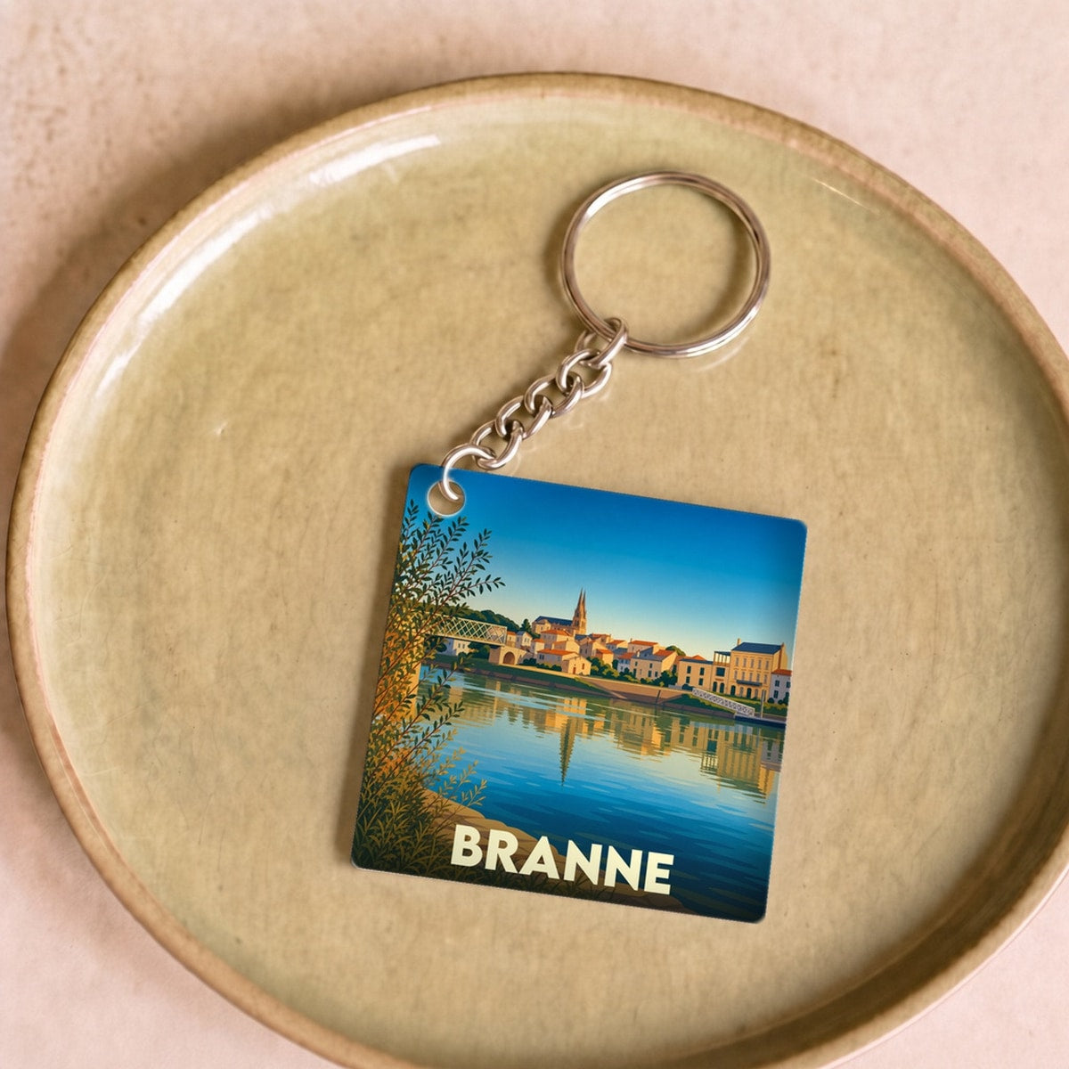 Porte-clés souvenir de la ville de Branne avec une illustration stylisée d'un paysage fluvial.