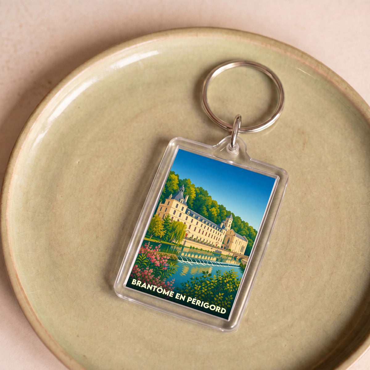 Porte-clés souvenir de la ville de Brantôme en Périgord avec une illustration stylisée de son abbaye au bord de l'eau.