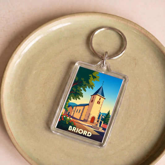 Porte-clés souvenir de la ville de Briord avec une illustration stylisée d'une église sous un ciel bleu.