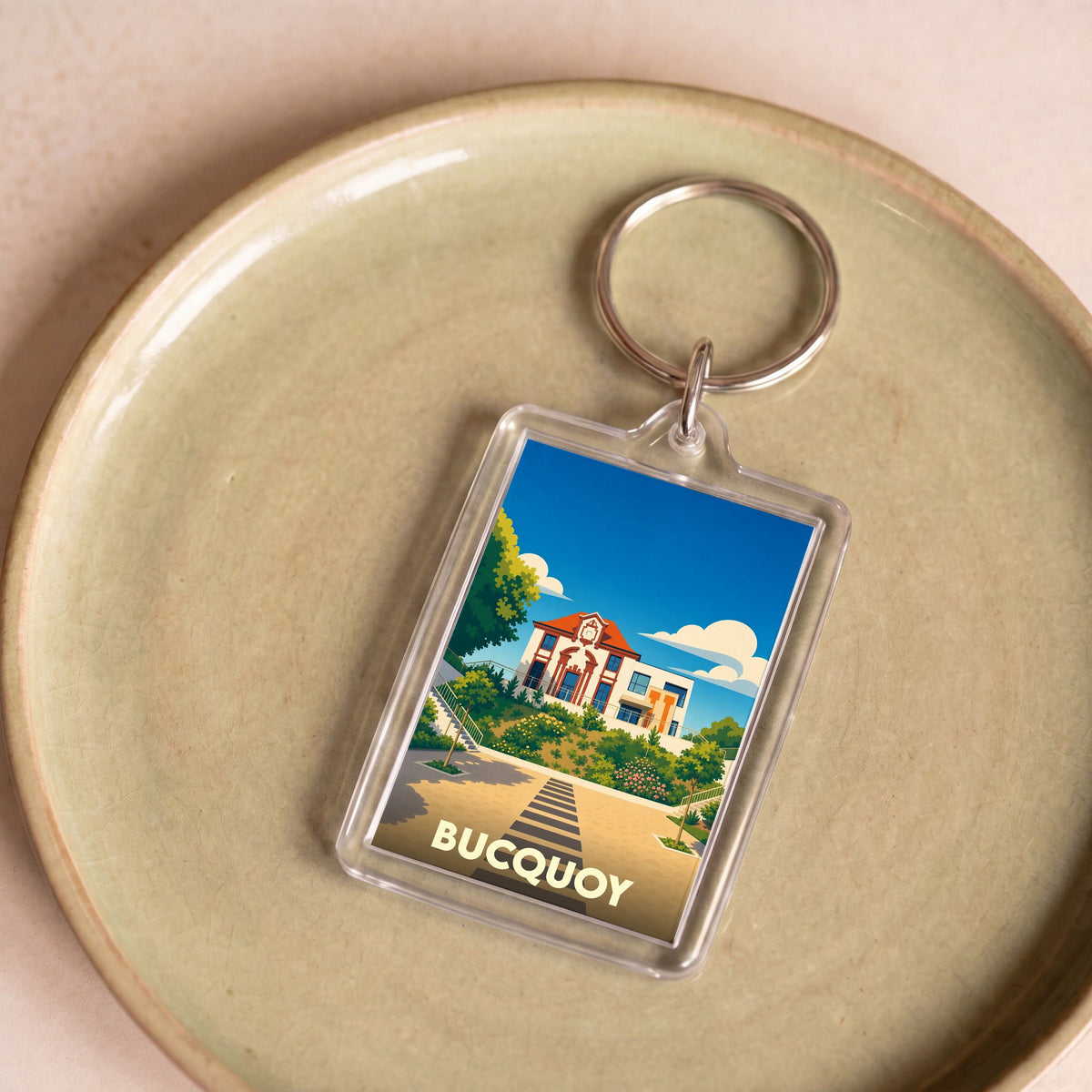 Porte-clés souvenir de la ville de Bucquoy avec une illustration stylisée d'un bâtiment emblématique.
