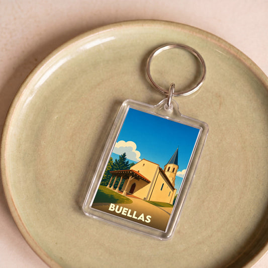 Porte-clés souvenir de la ville de Buellas avec une illustration stylisée d'une église sous un ciel bleu.