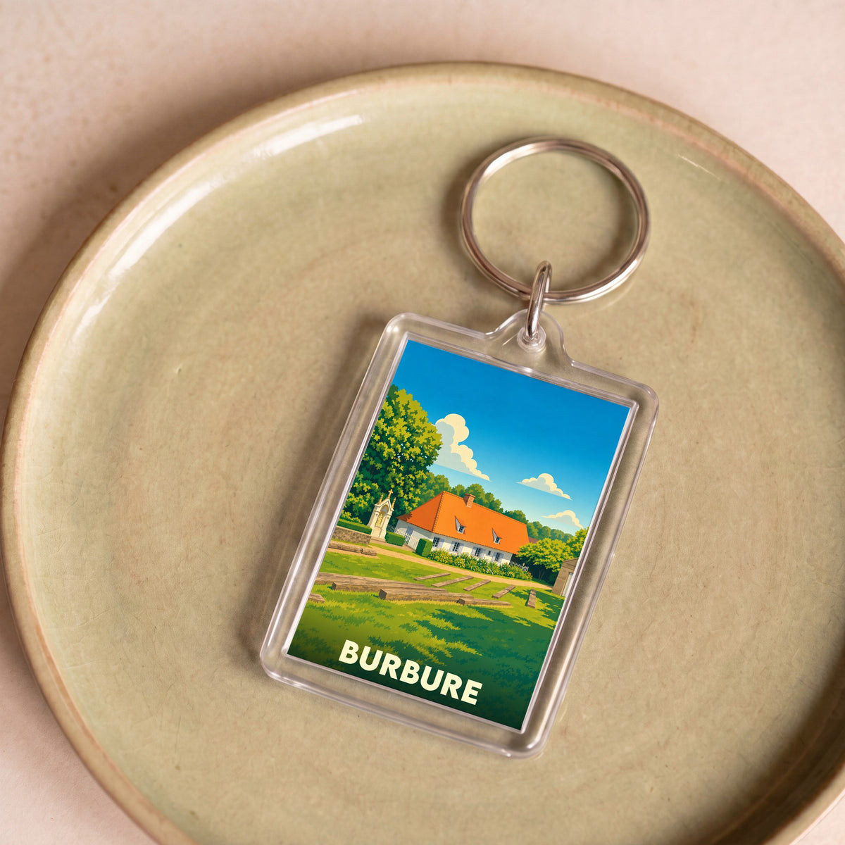 Porte-clés souvenir de la ville de Burbure avec une illustration stylisée d'une maison rurale sous un ciel bleu.