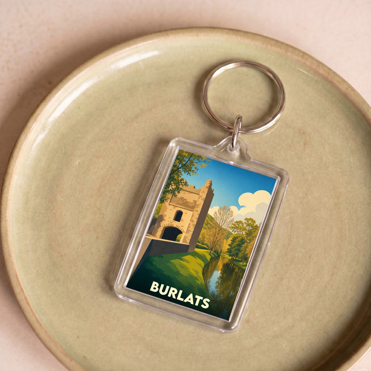 Porte-clés souvenir de la ville de Burlats avec une illustration stylisée d'un monument historique au bord de l'eau.