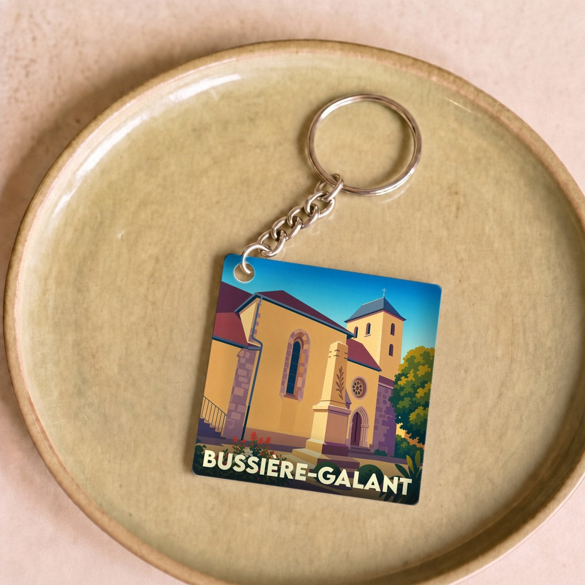 Porte-clés souvenir de la ville de Bussière-Galant avec une illustration stylisée de son église.