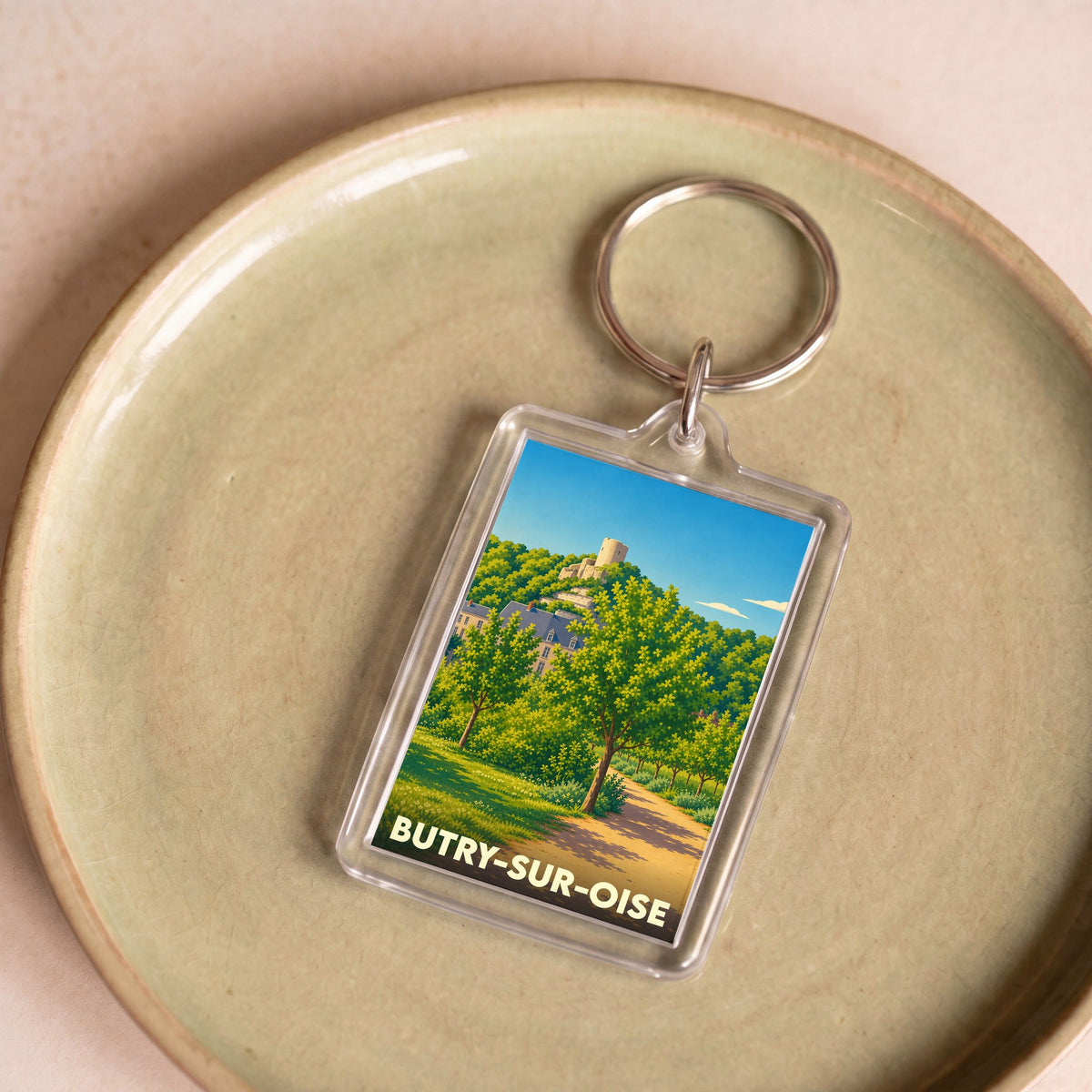 Porte-clés souvenir de la ville de Butry-sur-Oise avec une illustration stylisée d'un paysage verdoyant.