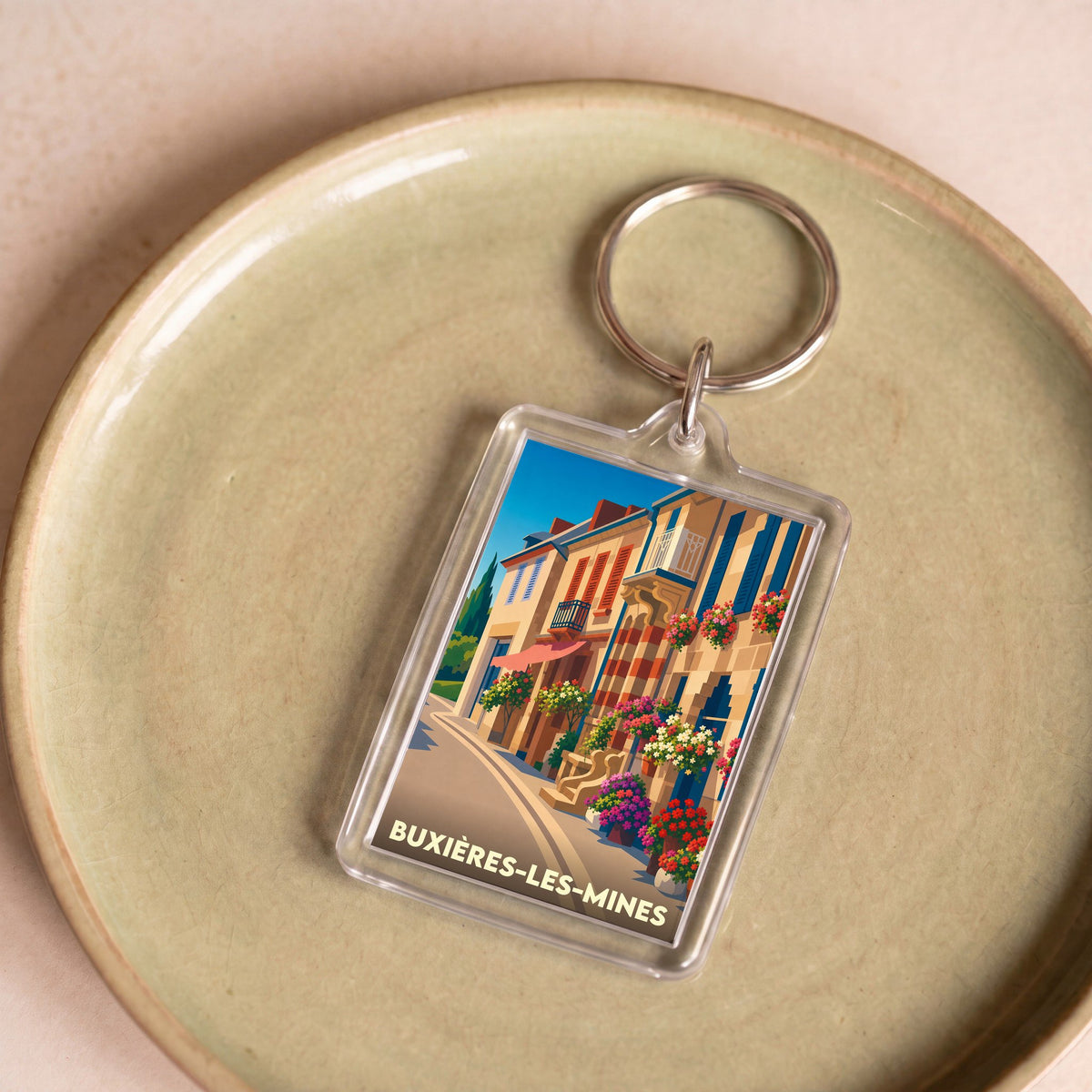 Porte-clés souvenir de la ville de Buxières-les-Mines avec une illustration colorée et stylisée d'une rue fleurie.