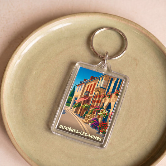 Porte-clés souvenir de la ville de Buxières-les-Mines avec une illustration colorée et stylisée d'une rue fleurie.