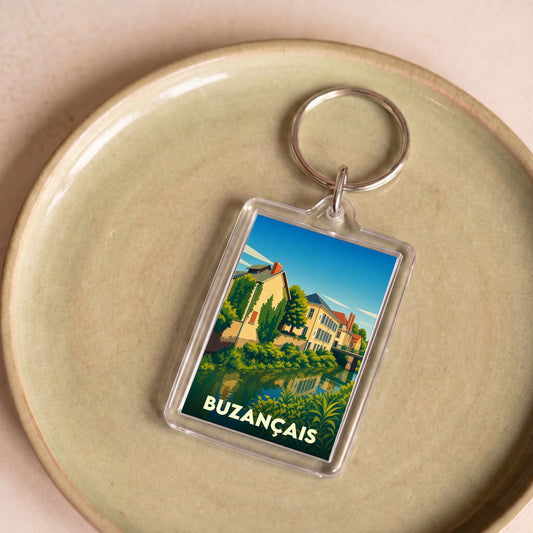 Porte-clés souvenir de la ville de Buzançais avec une illustration stylisée de bâtiments au bord de l'eau.
