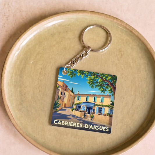 Porte-clés souvenir de la ville de Cabrières-d'Aigues avec une illustration stylisée d'une rue ensoleillée.