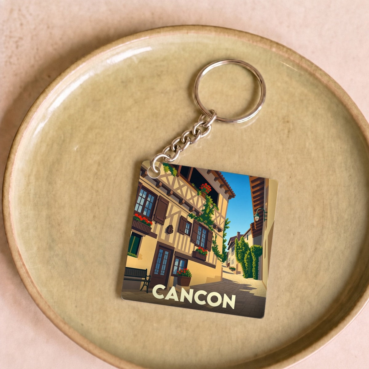 Porte-clés souvenir de la ville de Cancon avec une illustration stylisée d'une ruelle médiévale.