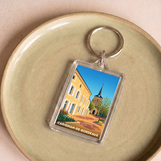 Porte-clés souvenir de Carignan-de-Bordeaux illustrant le centre du village dans un style graphique épuré.