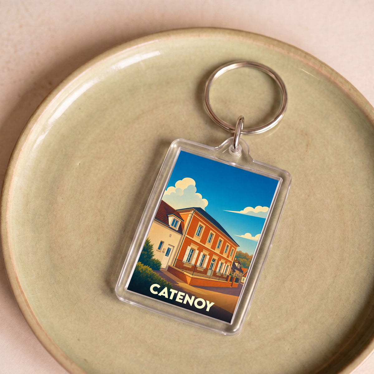 Porte-clés souvenir de la ville de Catenoy avec une illustration stylisée d'un bâtiment sous un ciel bleu.