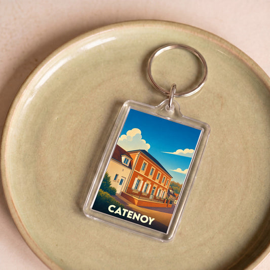 Porte-clés souvenir de la ville de Catenoy avec une illustration stylisée d'un bâtiment sous un ciel bleu.