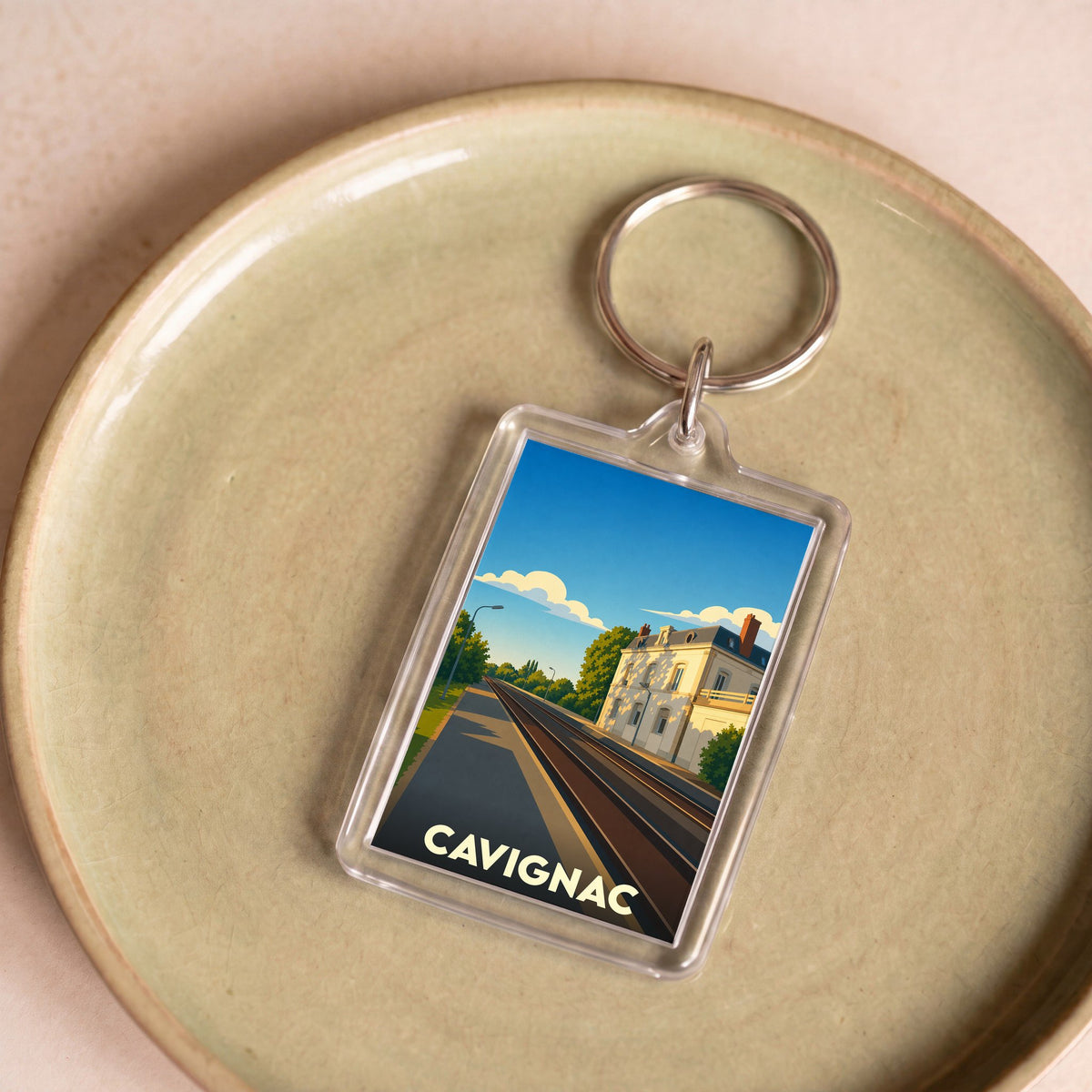 Porte-clés souvenir de la ville de Cavignac avec une illustration stylisée d'une gare sous un ciel bleu.