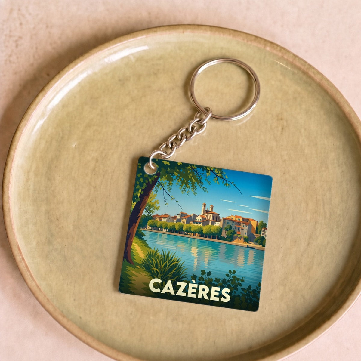 Porte-clés souvenir de la ville de Cazères avec une illustration stylisée d'un paysage fluvial.