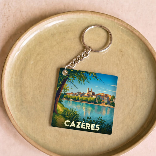 Porte-clés souvenir de la ville de Cazères avec une illustration stylisée d'un paysage fluvial.