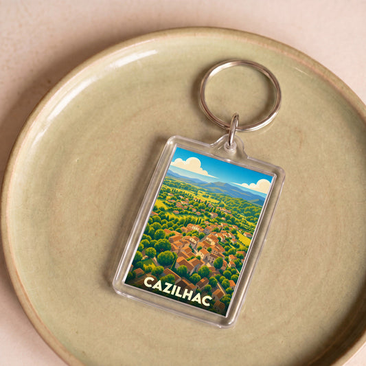 Porte-clés souvenir de la ville de Cazilhac avec une illustration stylisée d'un village niché dans une vallée verdoyante.
