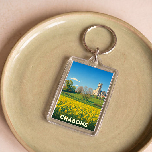 Porte-clés souvenir de la ville de Châbons avec une illustration stylisée d'un paysage champêtre et de son église.