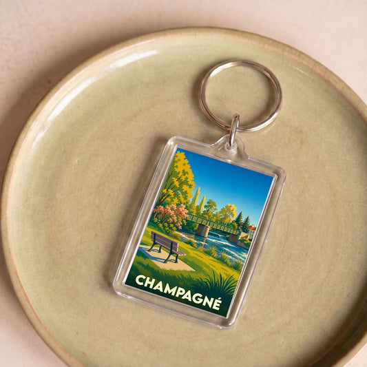 Porte-clés souvenir de la ville de Champagné avec une illustration stylisée d'un paysage de bord de rivière.