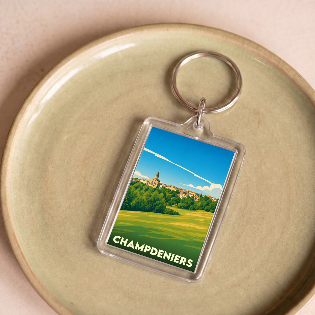 Porte-clés souvenir de la ville de Champdeniers avec une illustration stylisée de son paysage.