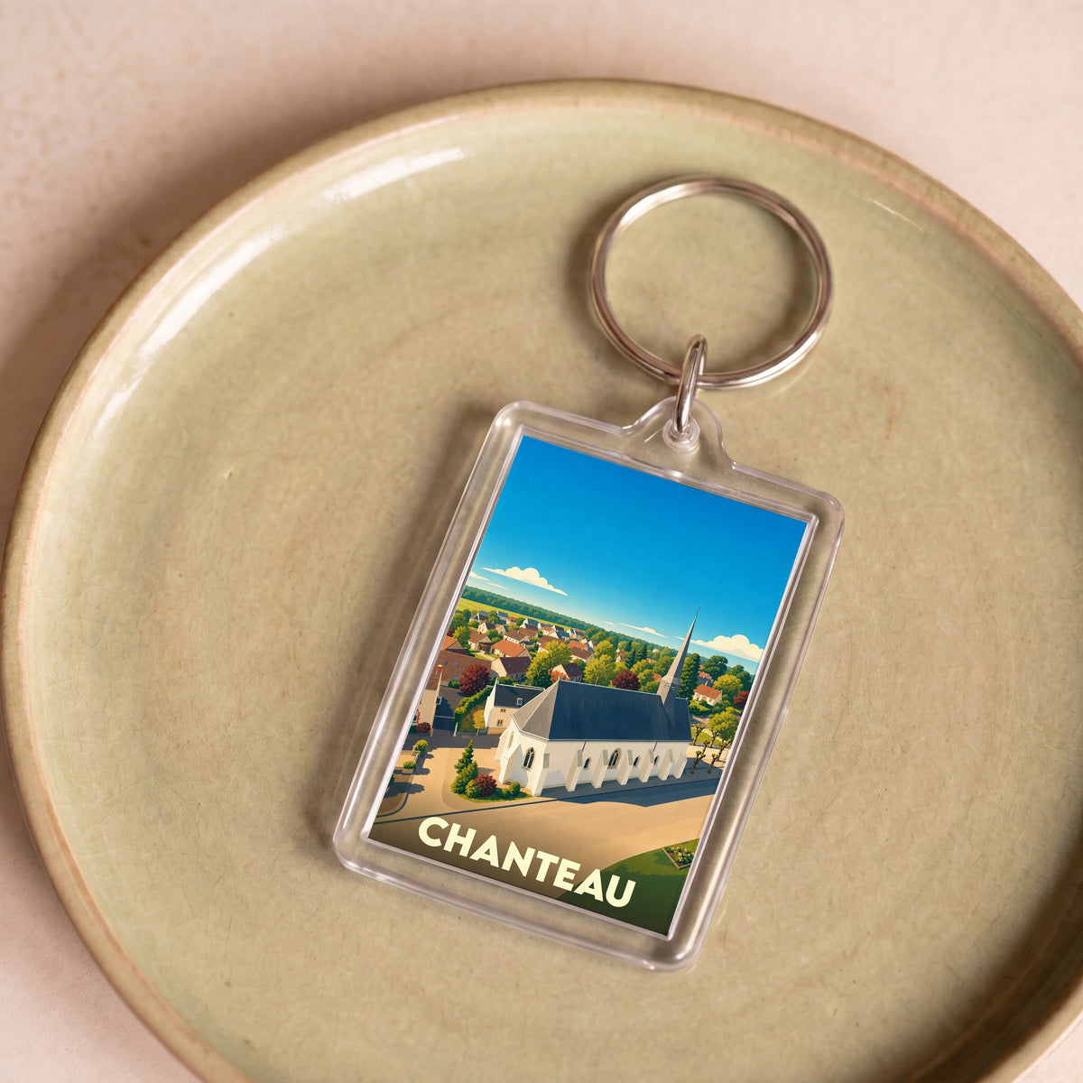 Porte-clés souvenir de la ville de Chanteau avec une illustration stylisée d'une église de campagne.
