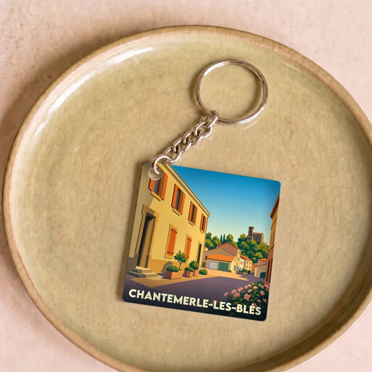 Porte-clés souvenir de la ville de Chantemerle-les-Blés avec une illustration stylisée d'une rue ensoleillée.