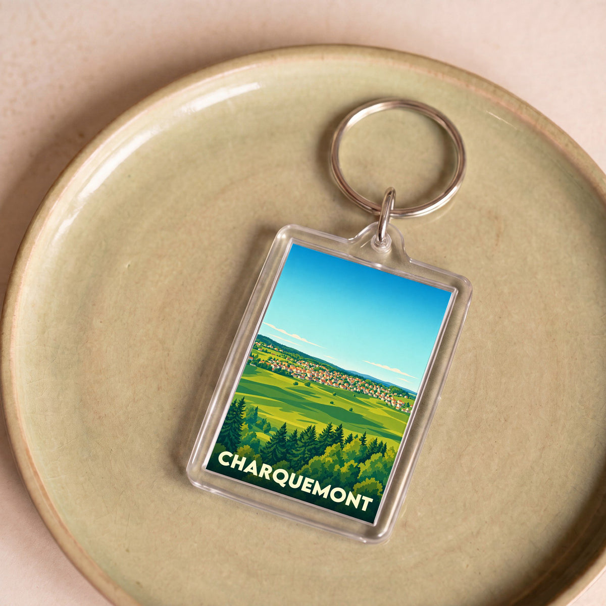 Porte-clés souvenir de la ville de Charquemont avec une illustration stylisée de son paysage champêtre.