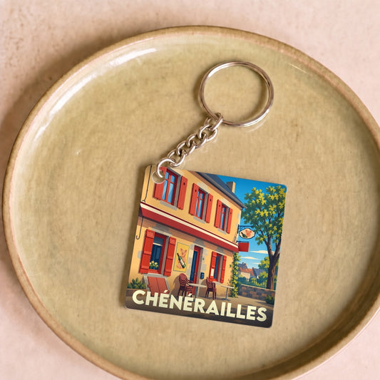 Porte-clés souvenir de la ville de Chénérailles avec une illustration stylisée d'une façade colorée.