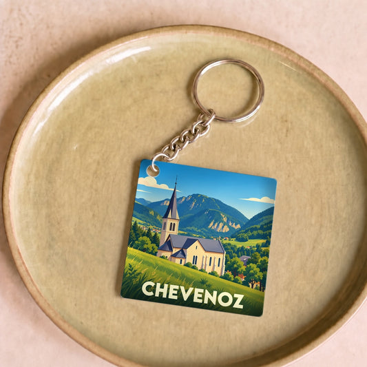 Porte-clés souvenir de la ville de Chevenoz avec une illustration stylisée de son église et des montagnes environnantes.